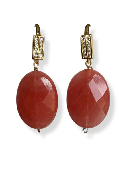Pair of earrings with red stones and gold accents on a white background