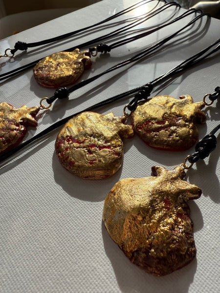 Gold-colored pomegranate pendants on black cords against a light gray background inamullumani wearable art