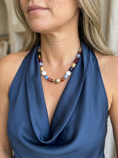 A close-up of a woman wearing a multi-colored beaded necklace with a central gold-toned bead, paired with a navy blue halter top inamullumani .