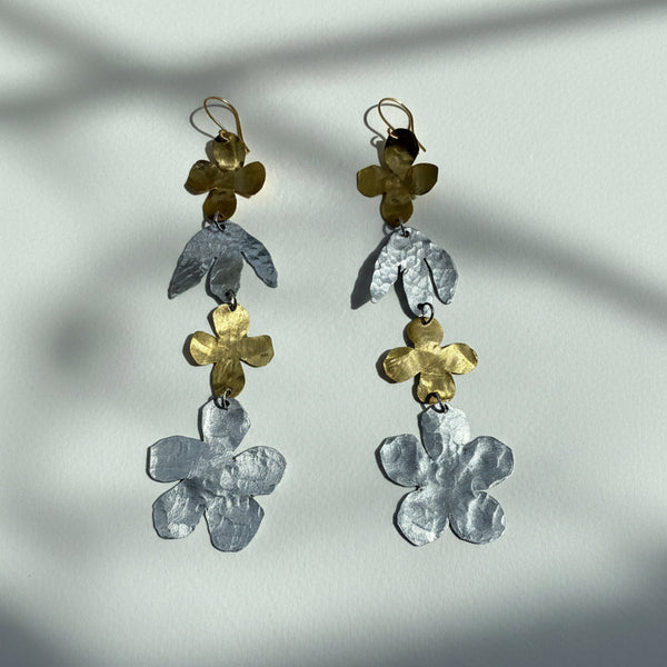 Pair of floral earrings shoulder duster with gold and silver flowers on a light backgrounds 