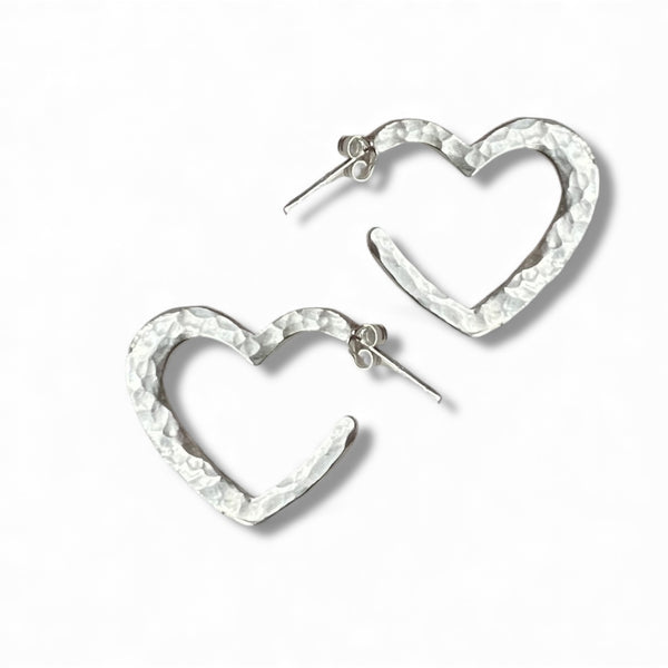 Pair of handmade sterling silver heart-shaped hoop earrings with a textured hammered finish on a white background.