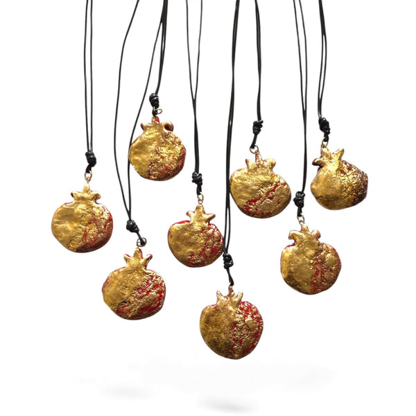 Gold pomegranate-shaped necklaces on black cords against a white background