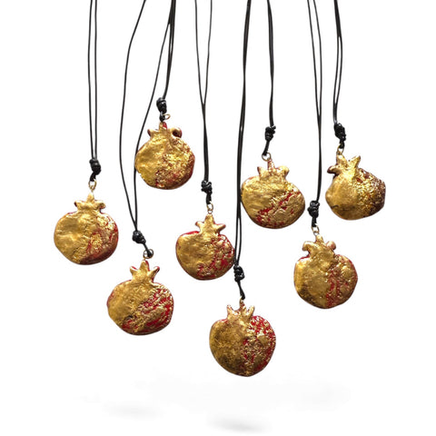 Gold pomegranate-shaped necklaces on black cords against a white background