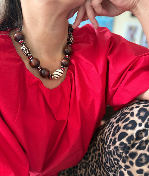 Person wearing a red shirt and leopard print pants with a chunky chocolate brown beaded necklace inamullumani 