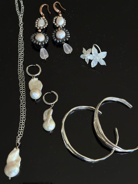 Collection of earrings including pearls and silver on a black background inamullumani 