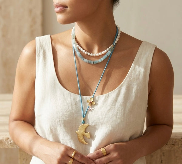 Woman wearing a necklace with a large dove gold pendant against a neutral background
