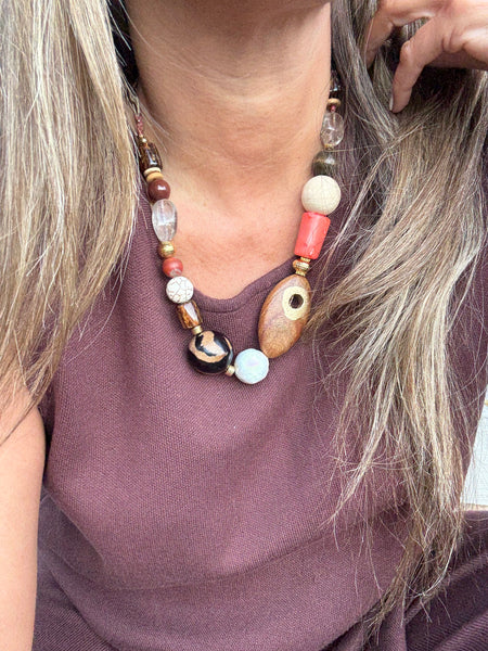 Close-up of a person wearing a big beaded handmade necklace on chocolate brown blouse with a blurred background