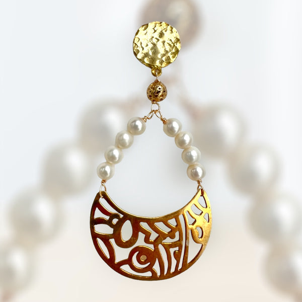 White pearl earring on white background with crescent shape with indigenous art designs gold plated silver and hammered finish inamullumani 