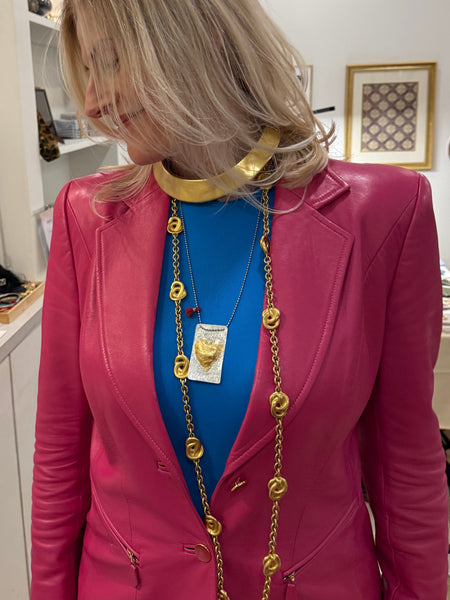 Person wearing a pink outfit with gold heart pendant and long gold necklace  in a room 