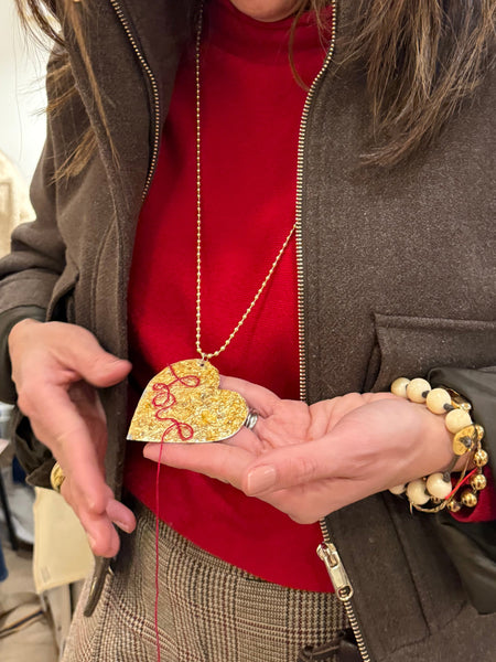 Woman holding a gold heart pendant with red thread  with a blurred background