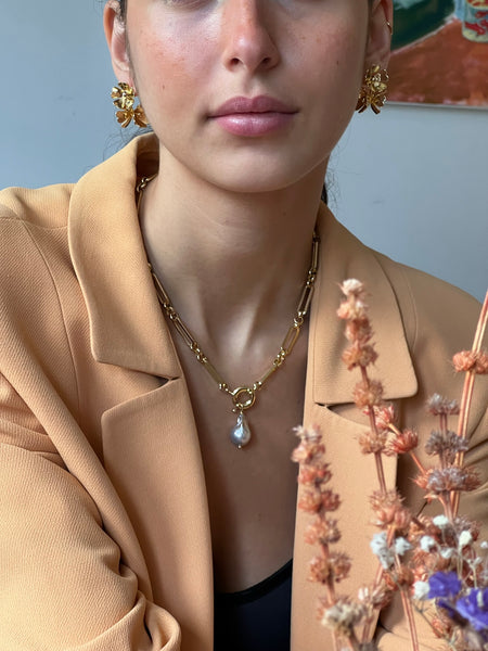 Woman in beige wearing flower earrings in gold and gold chain with baroque pearl 