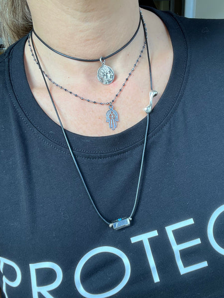 Person wearing layered necklaces with a visible brand logo on a dark shirt.